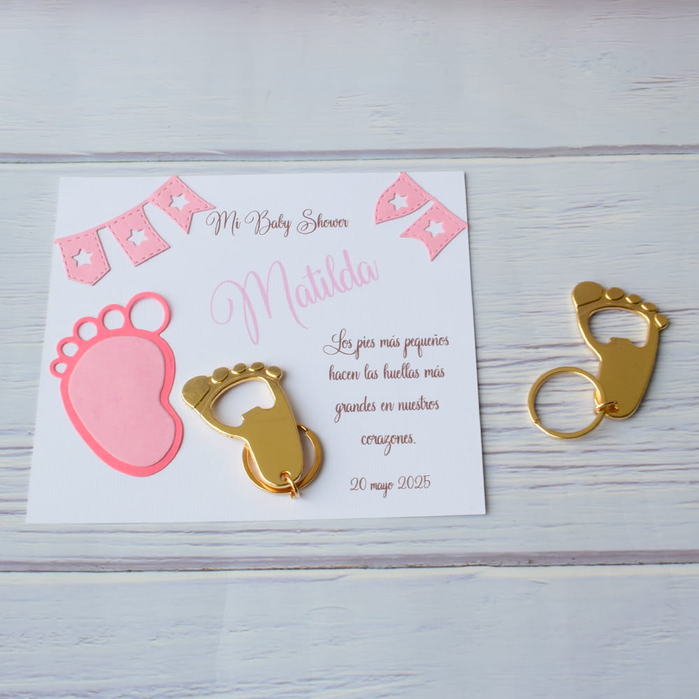 Llavero y destapador de metal dorado en forma de piecito junto a una tarjeta personalizada con detalles rosas, ideal para recuerdo de baby shower de niña en CDMX.