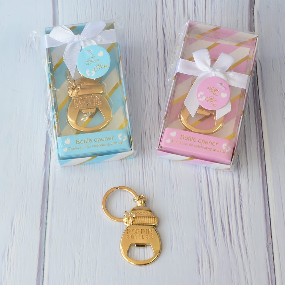 Recuerdos originales y útiles para Baby Shower. Llavero destapador dorado en forma de biberón. Muestra la presentación final del producto en prácticas cajas de regalo azul y rosa con listón, listos para entregar a los invitados del evento.