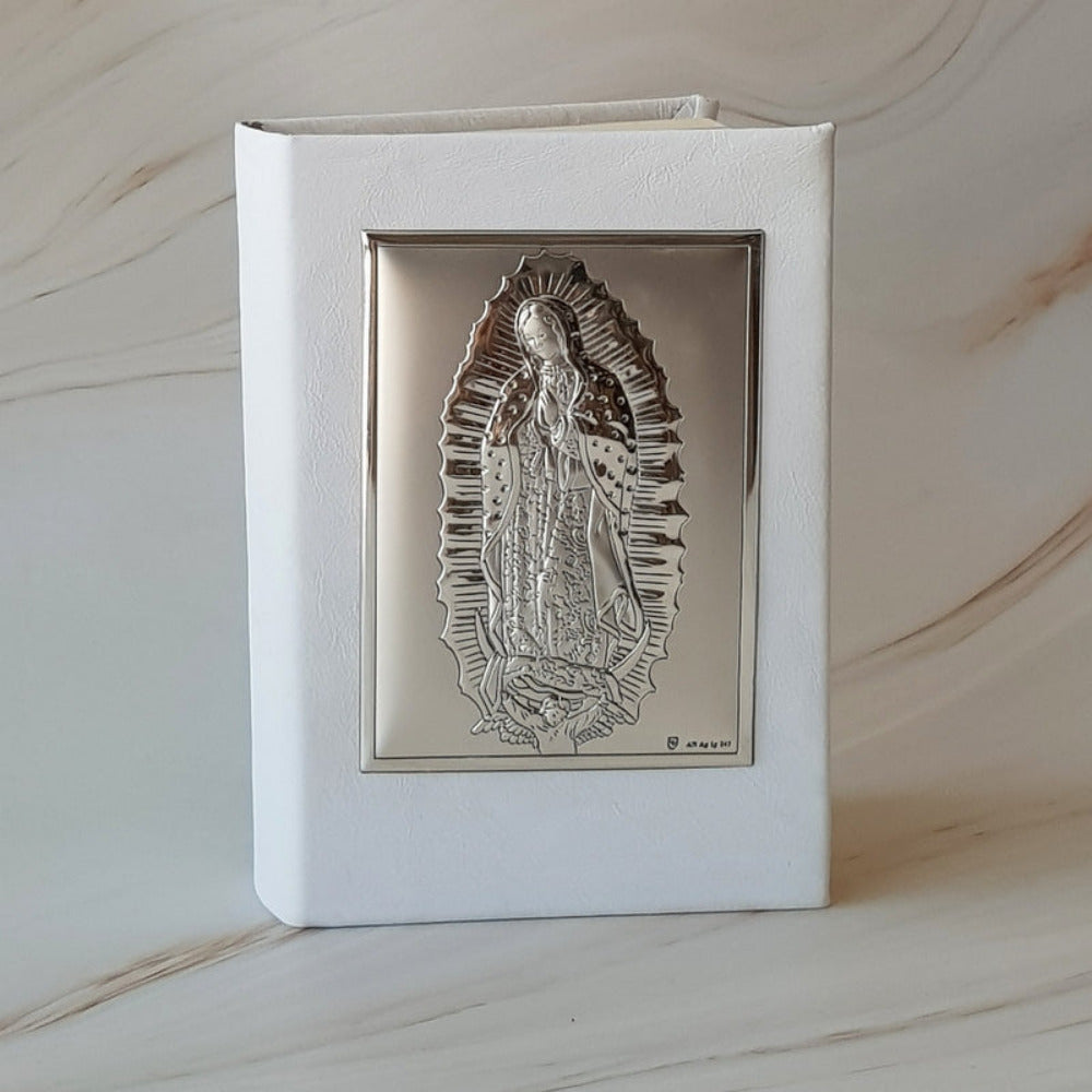 Biblia blanca para eventos con placa de plata de la Virgen de Guadalupe en relieve sobre fondo de mármol.