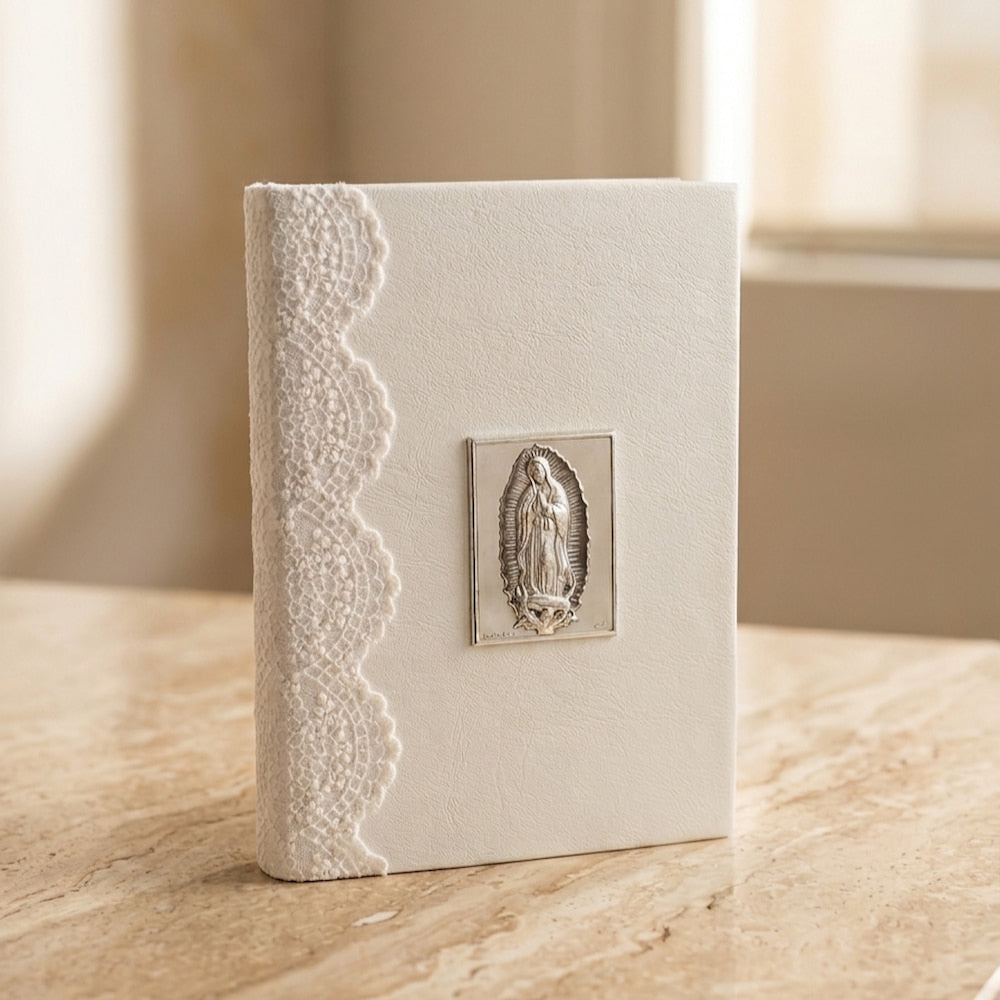 Biblia de boda con forro blanco texturizado, detalle de encaje lateral y placa de plata de la Virgen de Guadalupe.