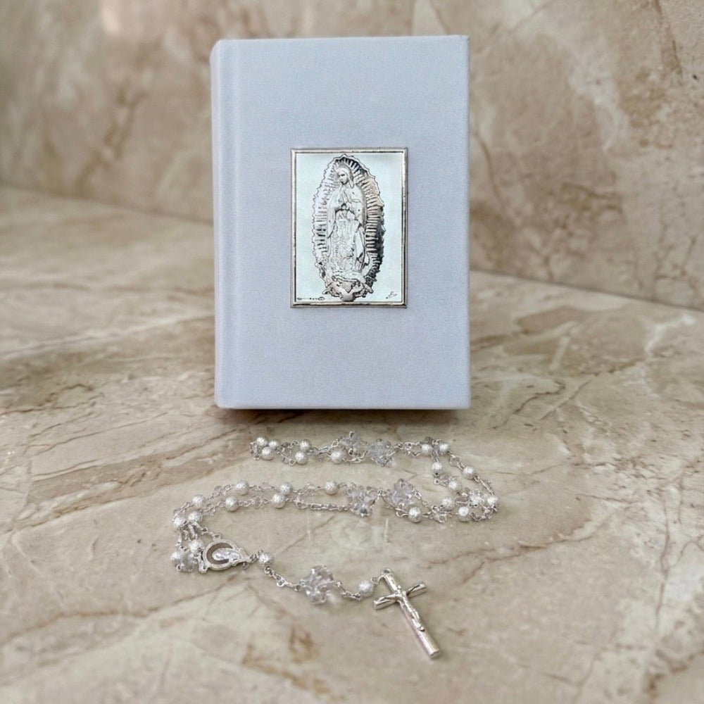 Biblia blanca con placa de la Virgen de Guadalupe y rosario plateado.