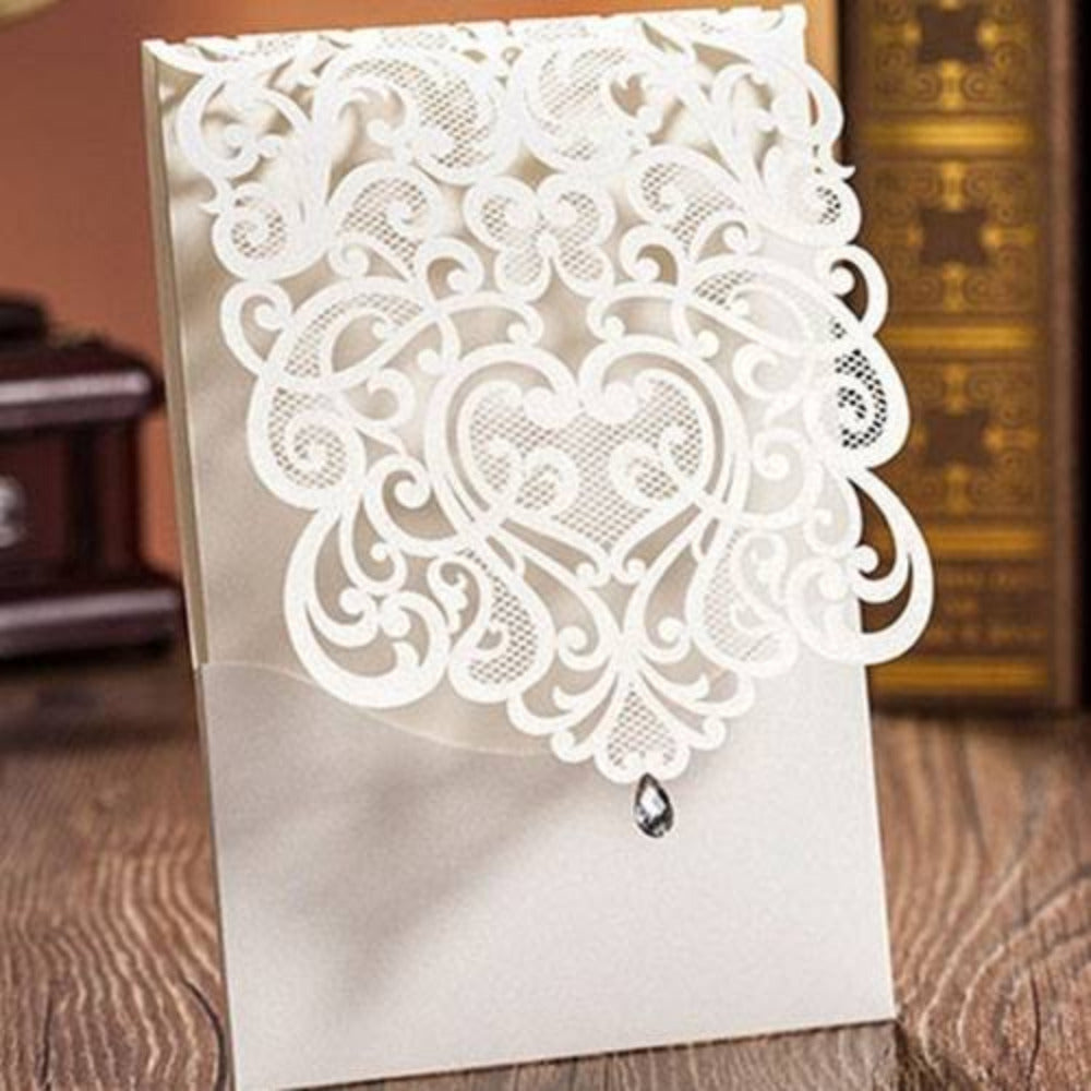 Invitación de boda elegante con diseño de corazón en corte láser color blanco perla, detalle de cristal colgante y texturas de encaje, papelería personalizada.