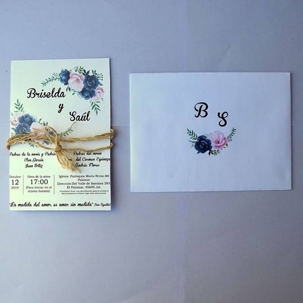 Invitación de boda con diseño floral de rosas en azul marino y rosa, decorada con lazo de ixtle rústico y sobre a juego con iniciales.