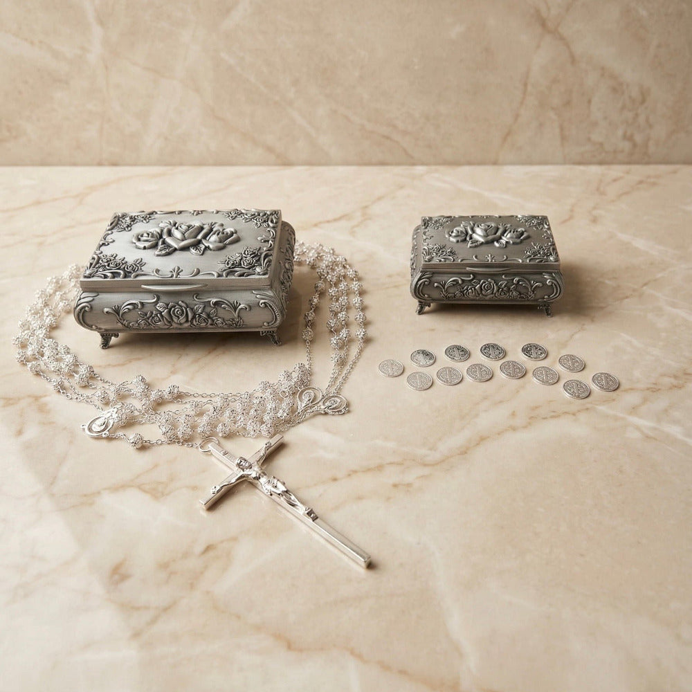 Set de accesorios para boda religiosa que incluye un lazo plateado estilo rosario con crucifijo, 13 arras matrimoniales y dos cofres rectangulares metálicos con relieve floral sobre una superficie de mármol.