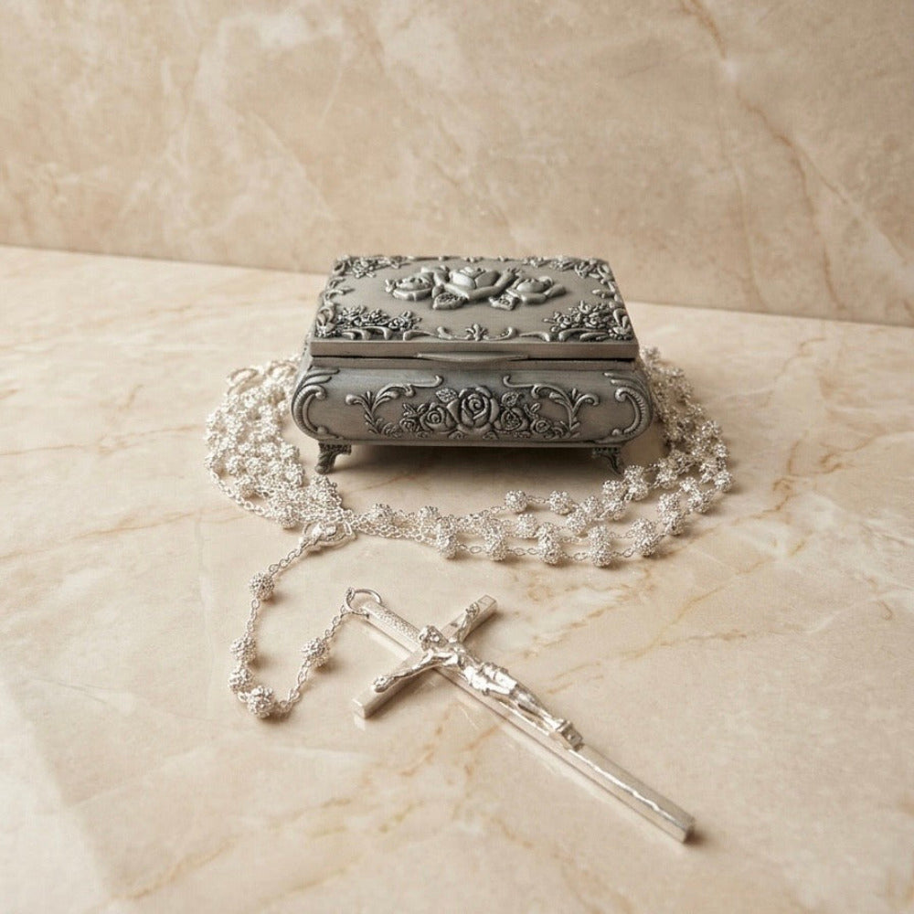 Rosario plateado con cruz y alhajero metálico con diseño de rosas en relieve, ideal para recuerdo de eventos religiosos.