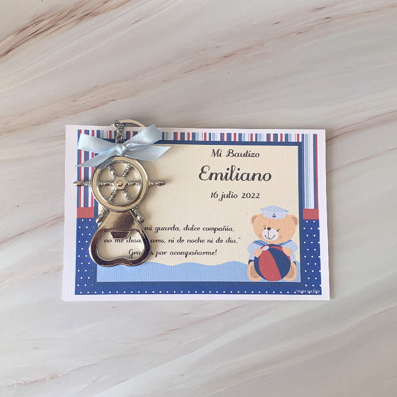 Llavero destapador metálico con diseño de timón náutico, ideal para recuerdos de eventos sociales, sobre fondo de mármol.