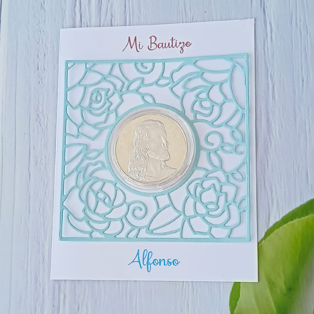 Tarjeta de recuerdo de bautizo para 'Alfonso', decorada con un marco de papel celeste calado y una moneda central con el perfil de Jesucristo.