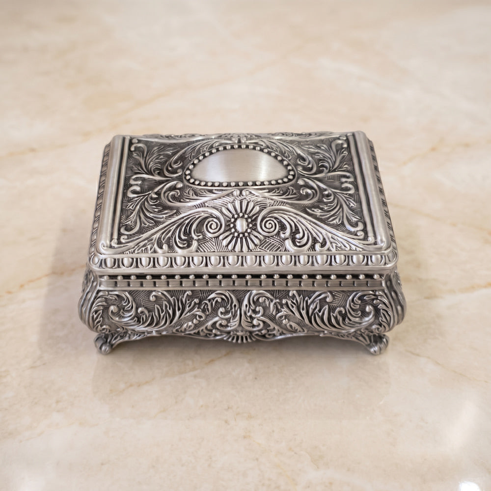 Cofre vintage de pewter para bodas con diseño floral en relieve y acabado antiguo sobre fondo de mármol.