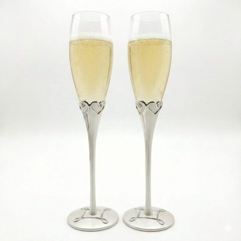 Set de dos copas para brindis de novios con tallos metálicos plateados y detalle de corazones en la base del cáliz, elegantes flautas de cristal para champaña en bodas y aniversarios.