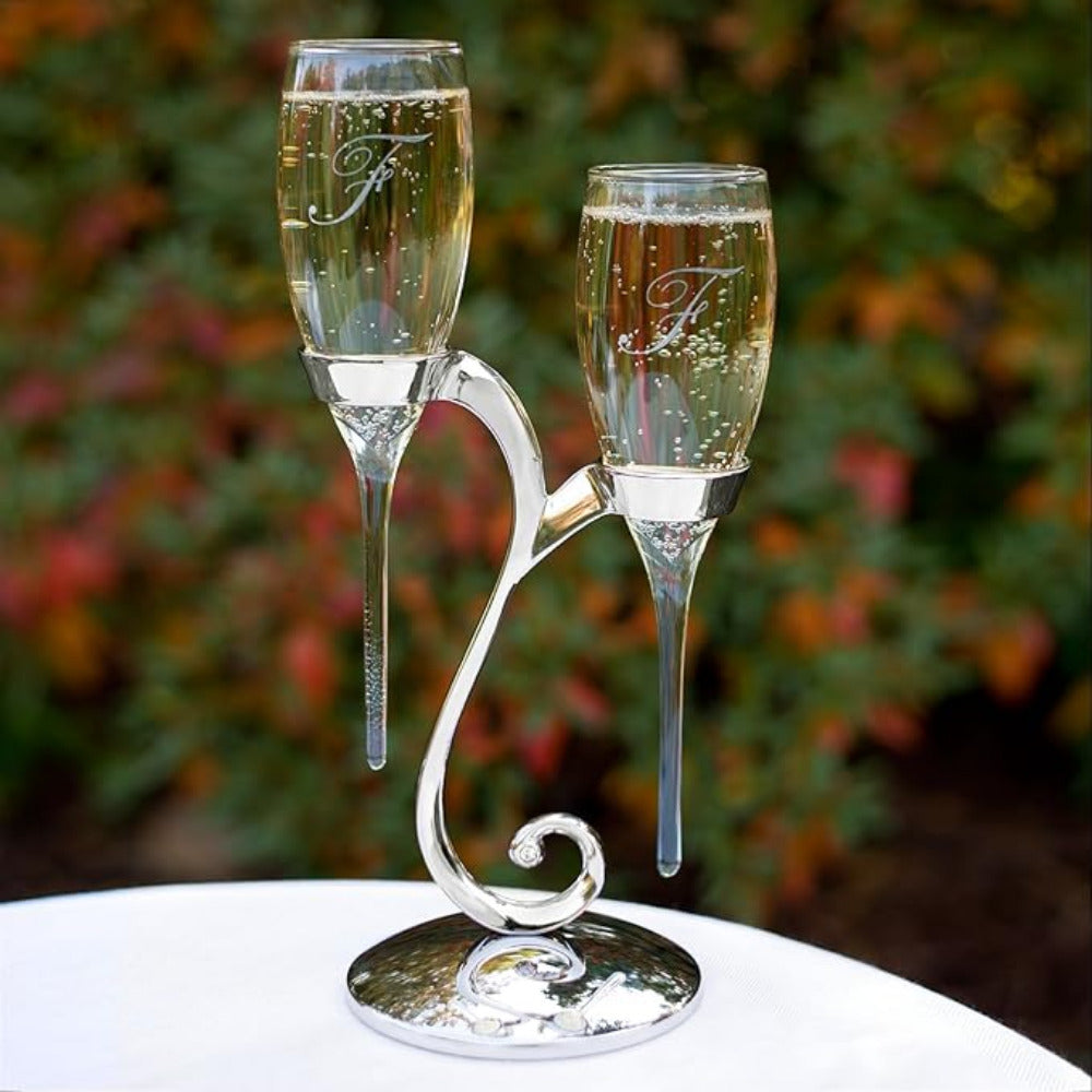 Set de dos copas para brindis nupcial con base compartida de diseño curvo en acabado plateado, flautas de cristal grabadas con iniciales para boda y aniversarios.