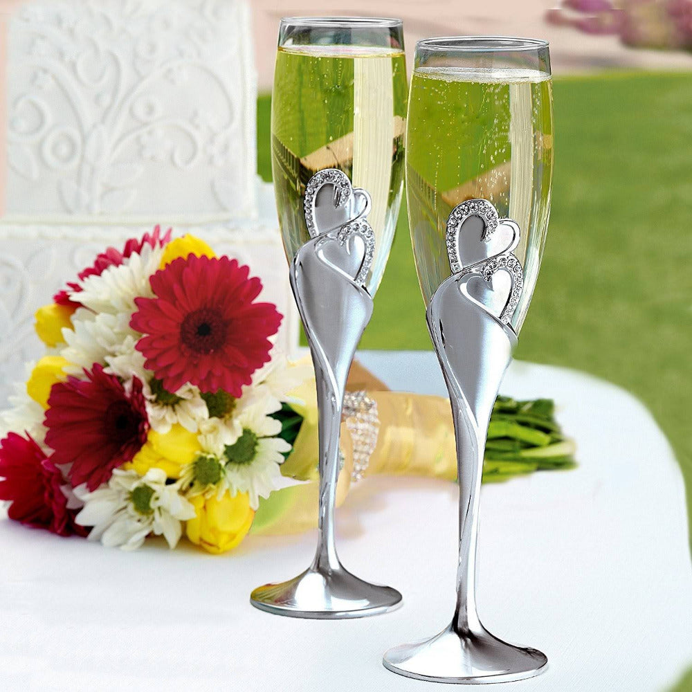 Juego de copas para brindis de boda con tallo plateado y diseño de corazones entrelazados con aplicaciones de pedrería, ideales para eventos nupciales.