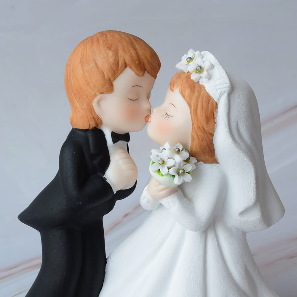 Figura para pastel de boda en primer plano de novios besándose, el novio con traje negro y la novia con vestido blanco sosteniendo un ramo de flores.