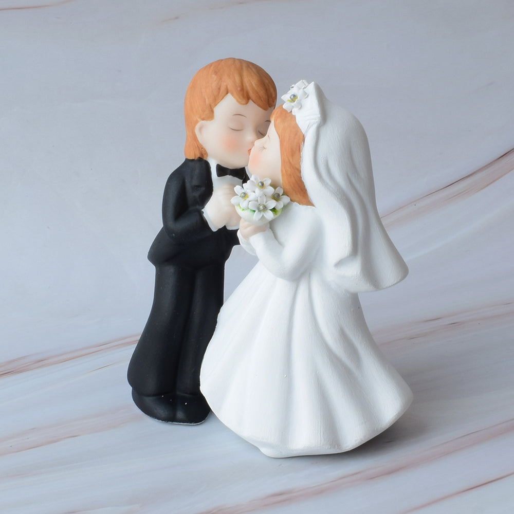Figura para pastel de bodas con pareja de novios dándose un beso sobre mármol.