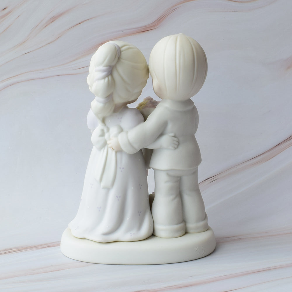 Figura para pastel de boda en cerámica con detalles de flores y la frase "Love Vows To Always Bloom", sobre fondo de mármol.