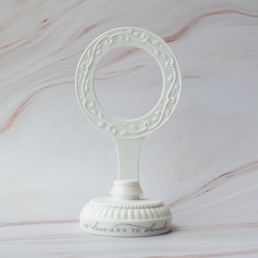 Base para figura de pastel en cerámica blanca con diseño circular y detalles de hojas en relieve sobre mármol.