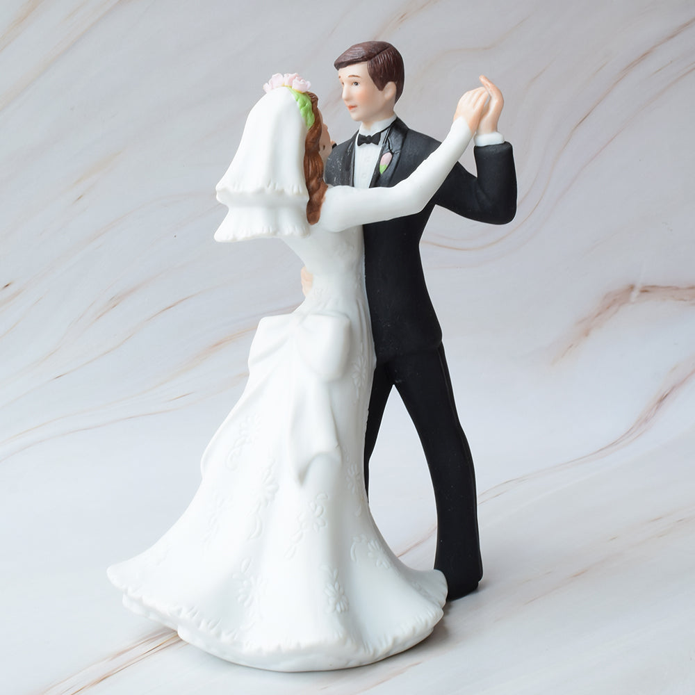 Figura para pastel de boda con novios bailando, ella con vestido de novia detallado y él con traje negro, sobre fondo de mármol.