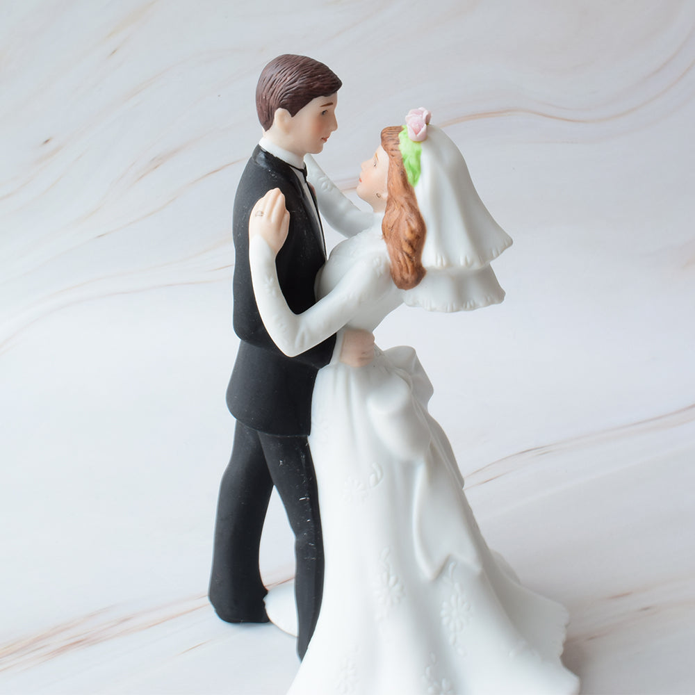 Figura para pastel de boda con novios bailando, ella con vestido de novia detallado y él con traje negro, sobre fondo de mármol.