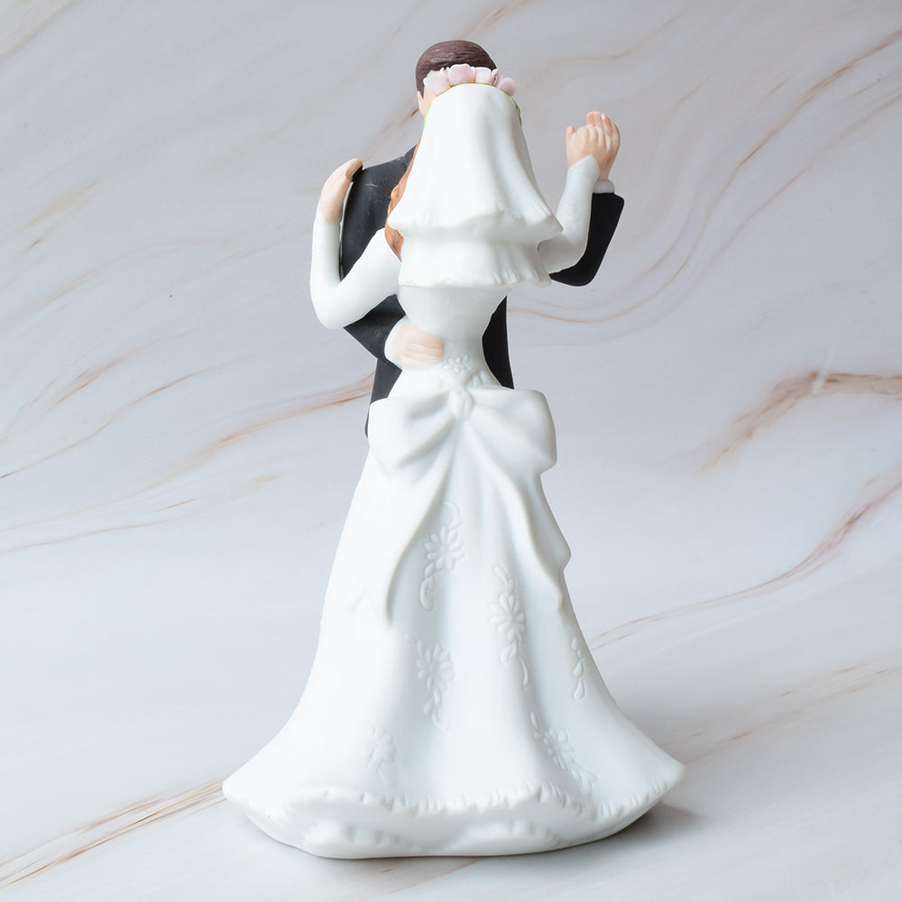 Figura para pastel de boda con novios bailando, ella con vestido de novia detallado y él con traje negro, sobre fondo de mármol.