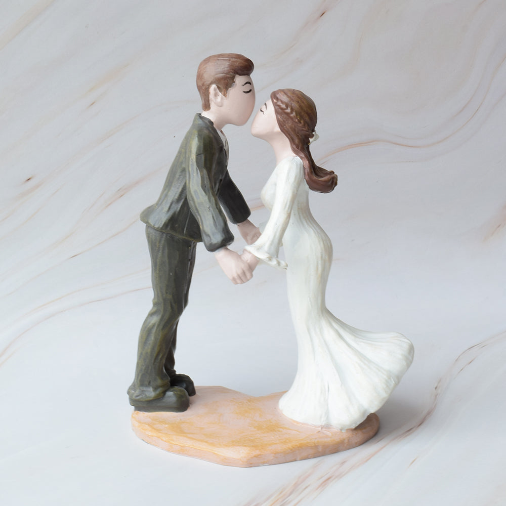 Figura para pastel de bodas en cerámica con novios dándose un dulce beso, sobre fondo de mármol.
