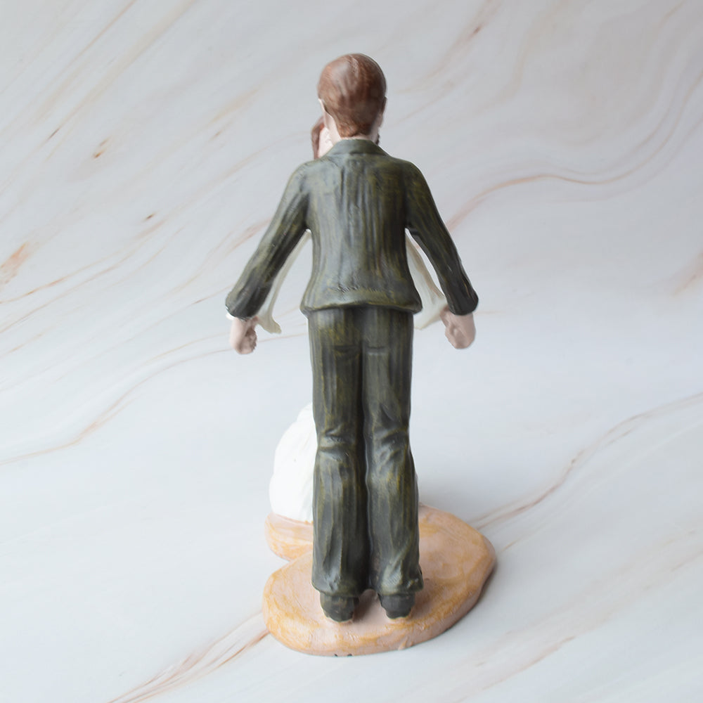 Figura para pastel de bodas en cerámica con novios dándose un dulce beso, sobre fondo de mármol.