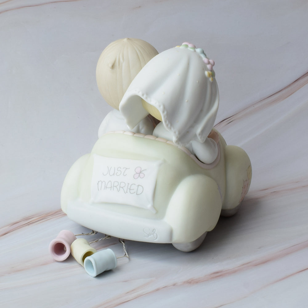 Figura para pastel Precious Moments con novios abrazados, estilo porcelana en tonos suaves, ideal para decoración de bodas elegantes.