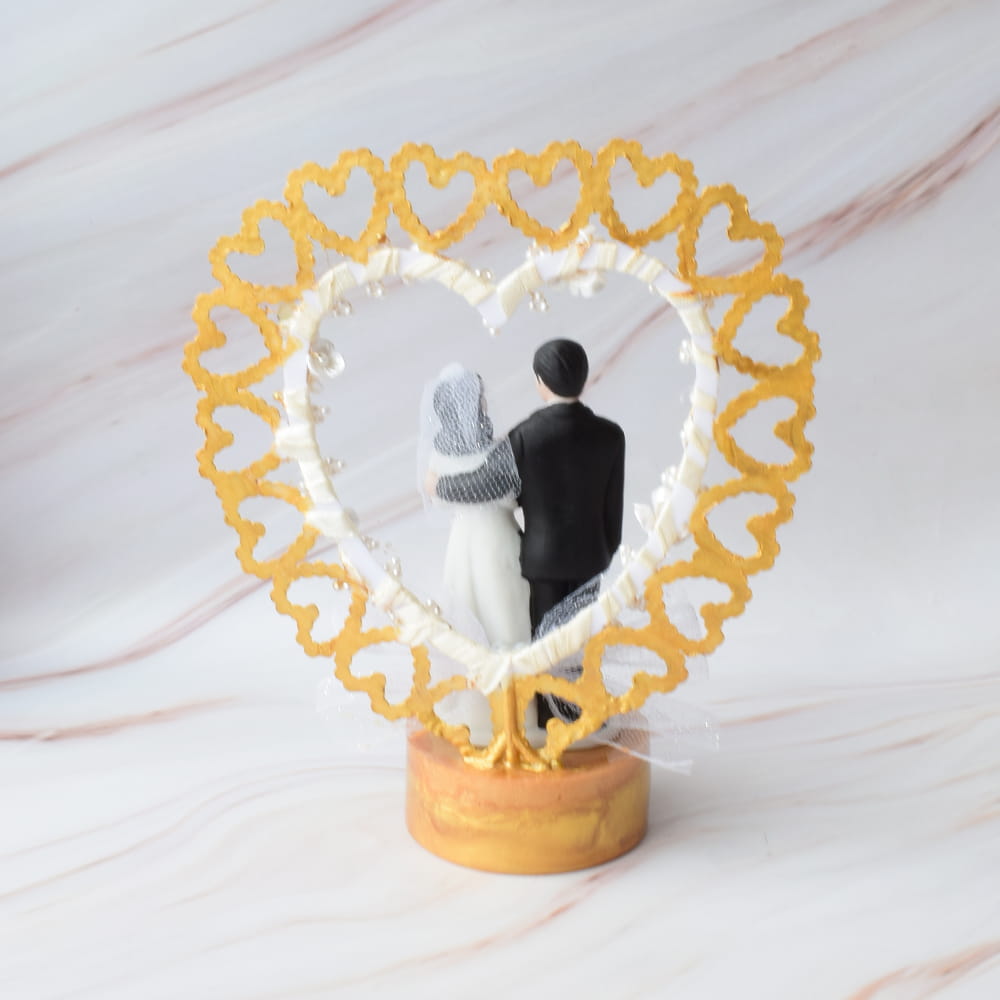 Figura para pastel de boda con novios abrazados dentro de un corazón dorado.
