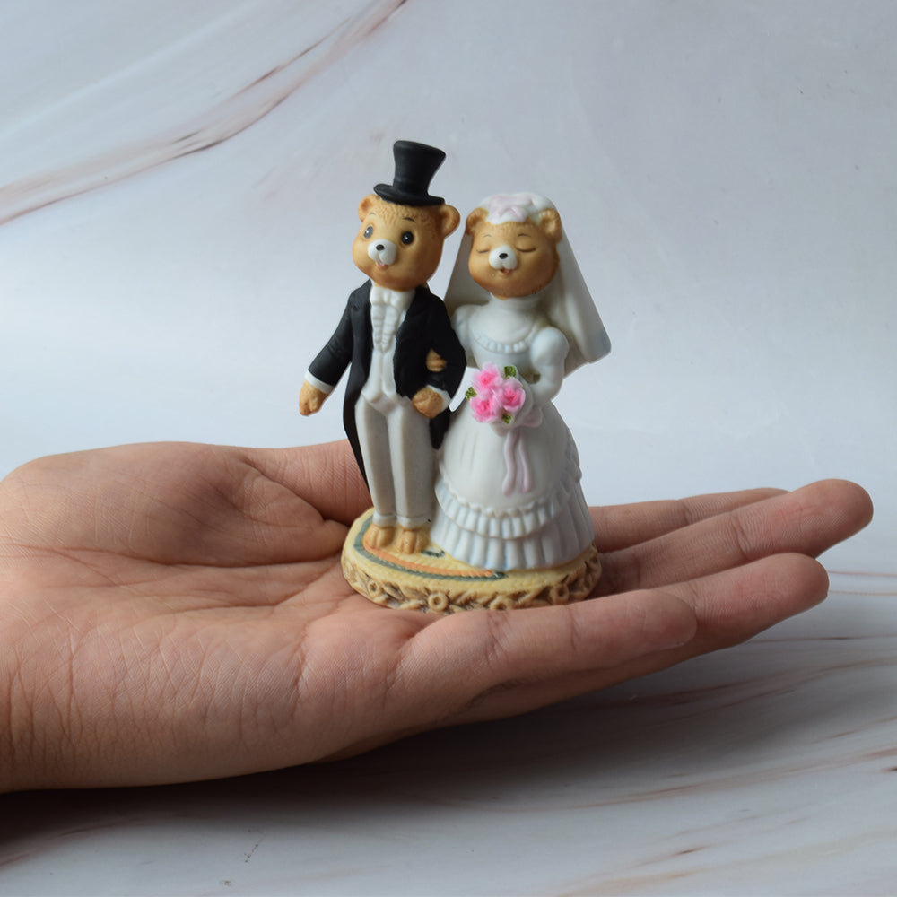 Figura para pastel de boda con pareja de ositos estilo caricatura, abrazados y con detalles florales, sobre fondo blanco.