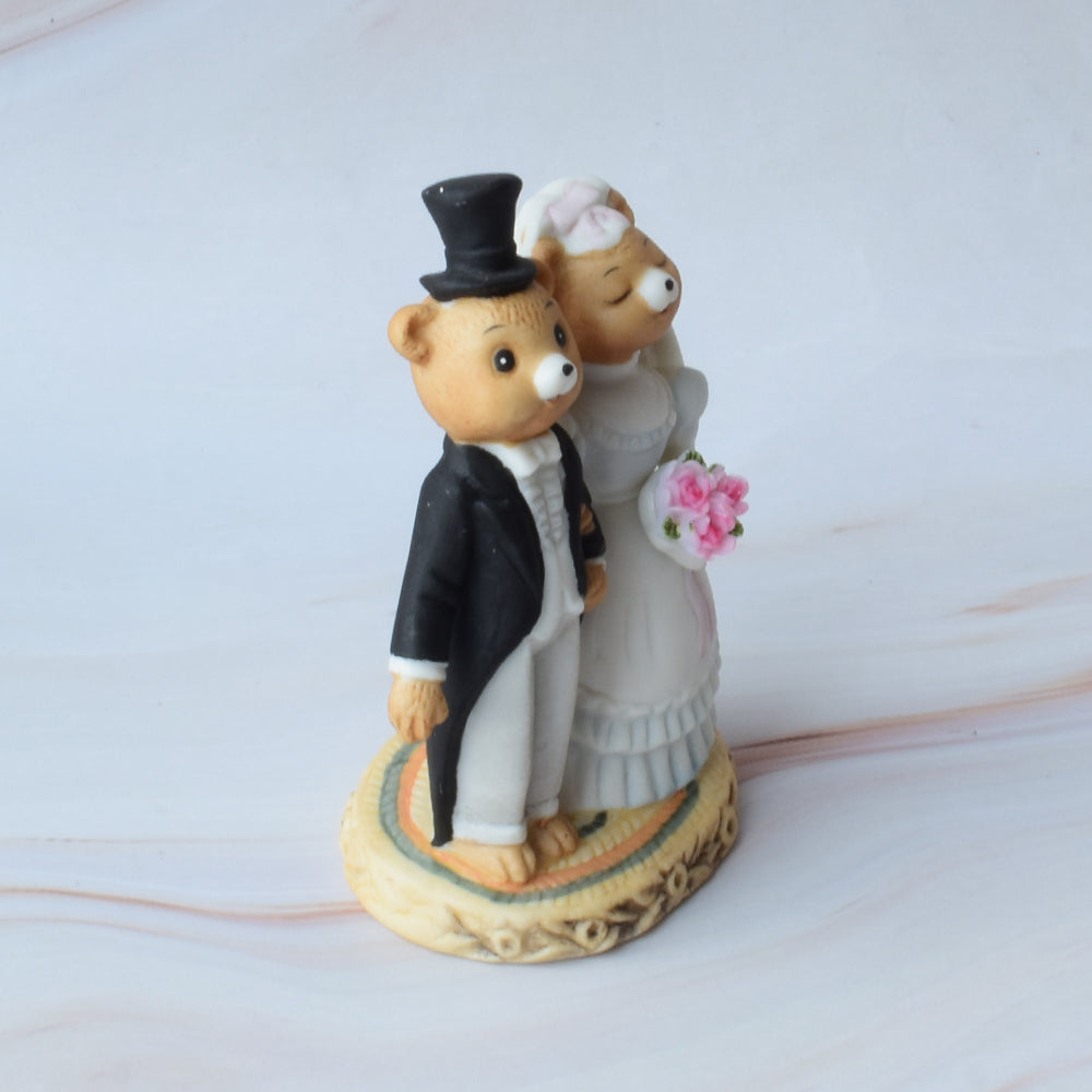 Figura para pastel de boda con pareja de ositos estilo caricatura, abrazados y con detalles florales, sobre fondo blanco.