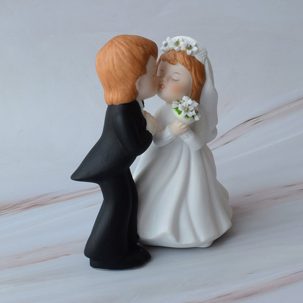 Figura para pastel de bodas con pareja de novios dándose un beso sobre mármol.