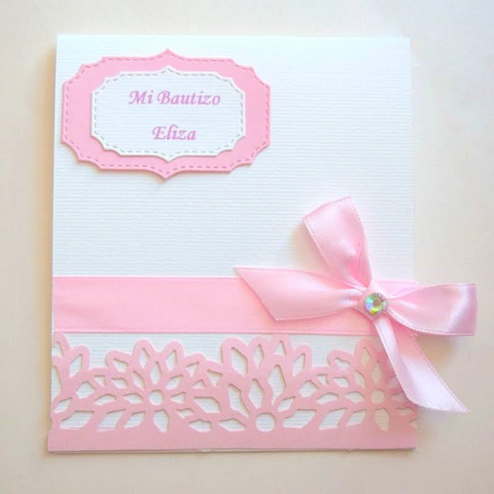 Invitación artesanal para bautizo de niña en color rosa y blanco con listón satinado, detalle de pedrería y borde calado floral, papelería personalizada para eventos.