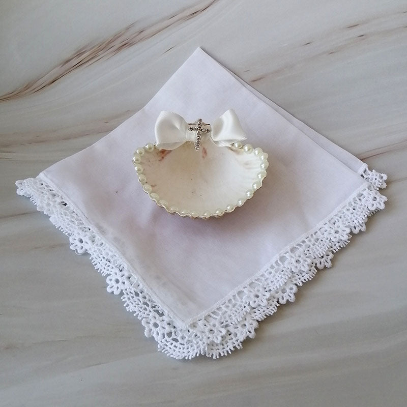 Kit de bautizo artesanal con pañuelo blanco de encaje, concha natural decorada y figura de monito sobre mármol.