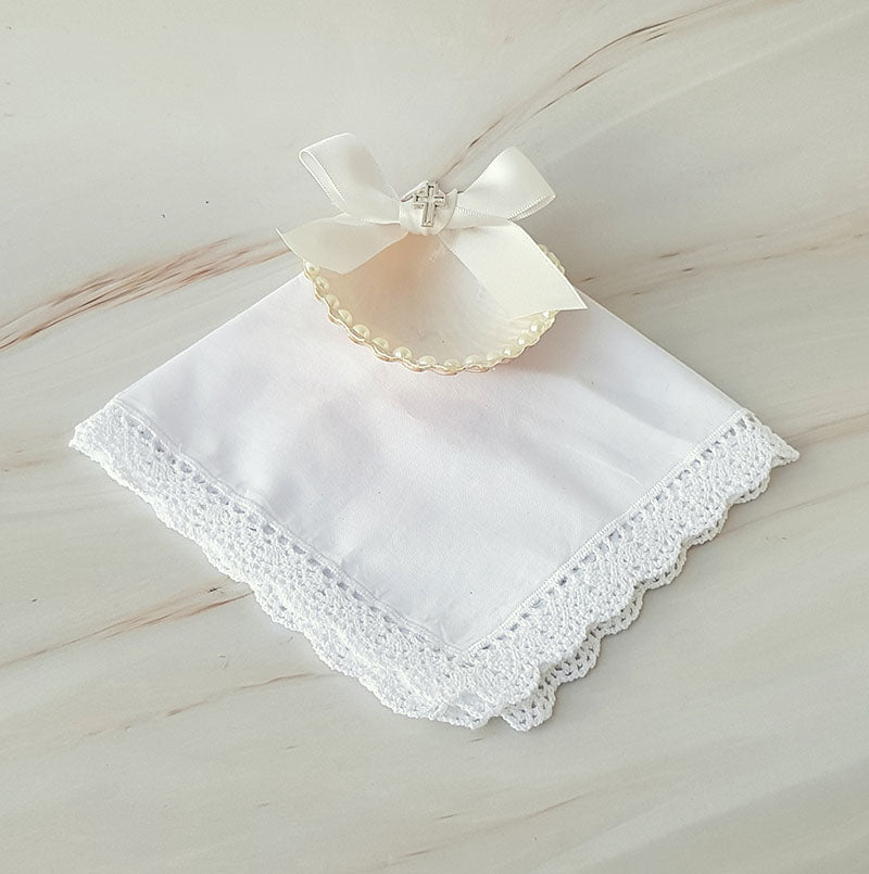 Kit de bautizo artesanal con pañuelo bordado, conchita natural y vela decorada con un pequeño mono sobre fondo blanco.
