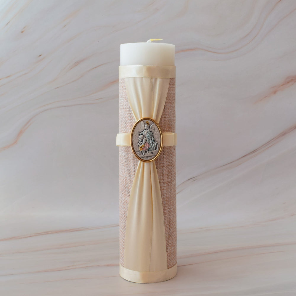 Cirio para bautizo forrado en yute con detalles de listón beige y medalla ovalada del Ángel de la Guarda sobre mármol.