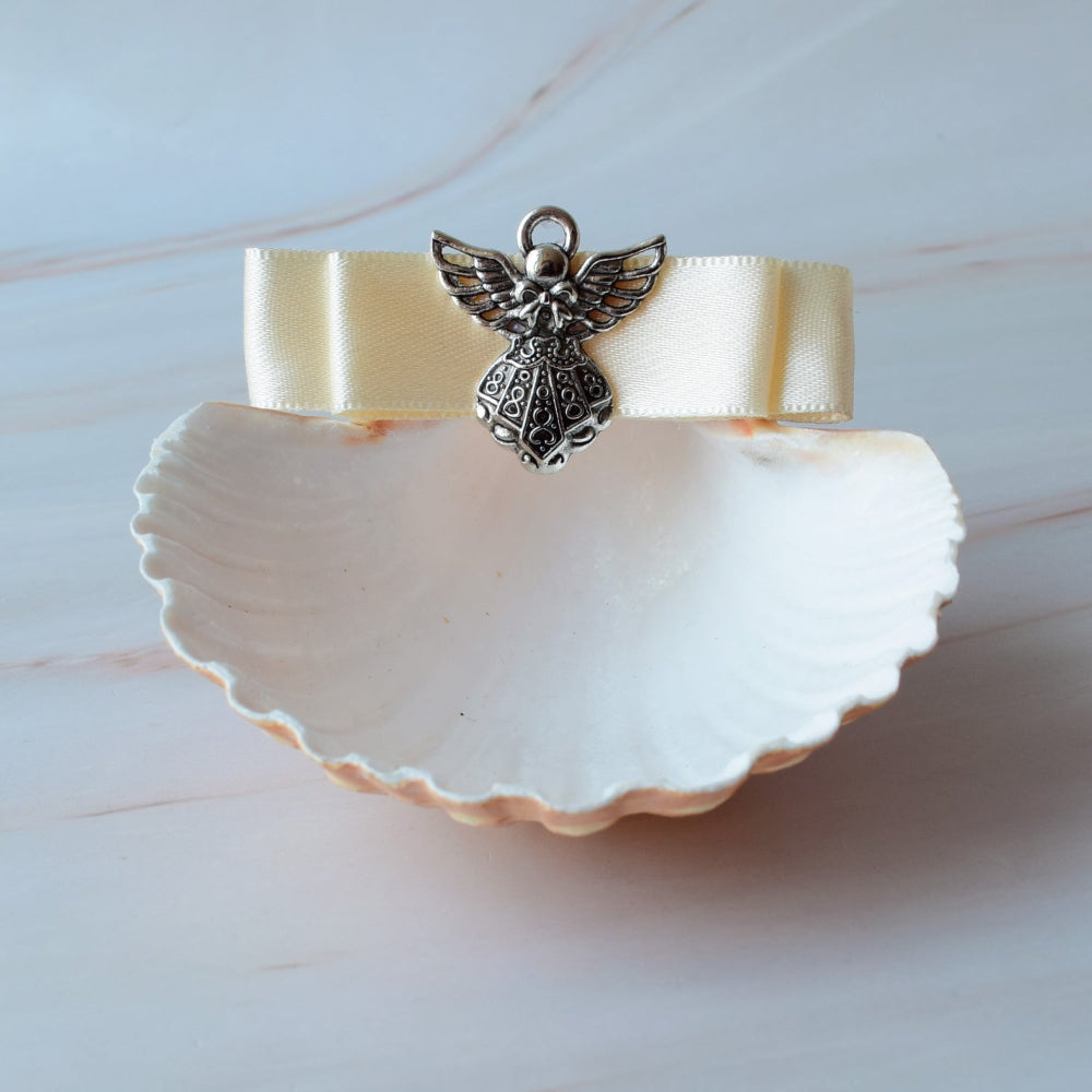 Concha natural para bautizo con moño satinado y dije de ángel metálico, accesorio artesanal elegante para ceremonias en México.