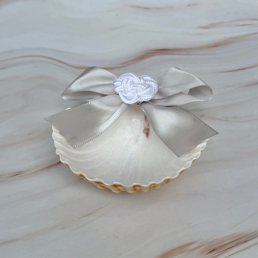Concha bautismal natural con moño de listón satinado plateado y detalle de nudo artesanal blanco para ceremonia de bautizo.