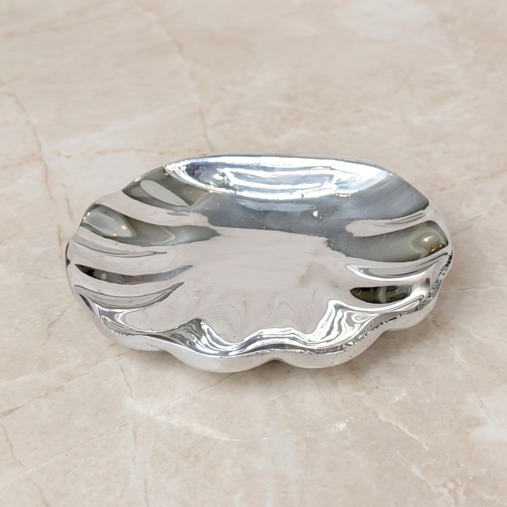 Concha de bautismo de pewter pulida con bordes ondulados sobre superficie de mármol.