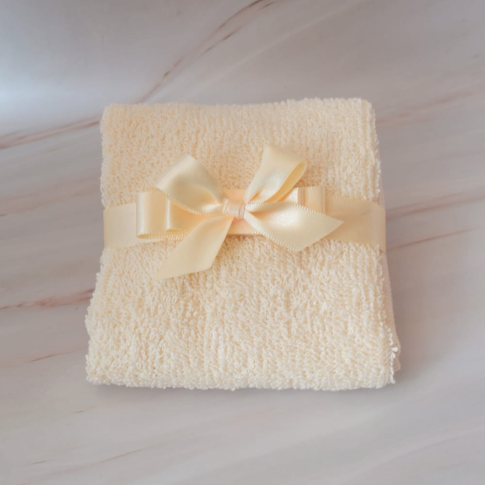 Toallita color beige doblada y decorada con un moño de listón a juego, ideal para kit de recuerdo de bautizo en CDMX.
