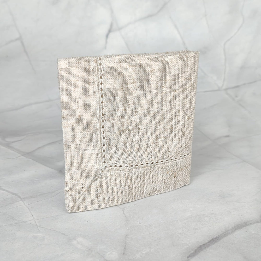 Pañito para bautizo en lino color beige con detalle bordado sobre mármol gris.