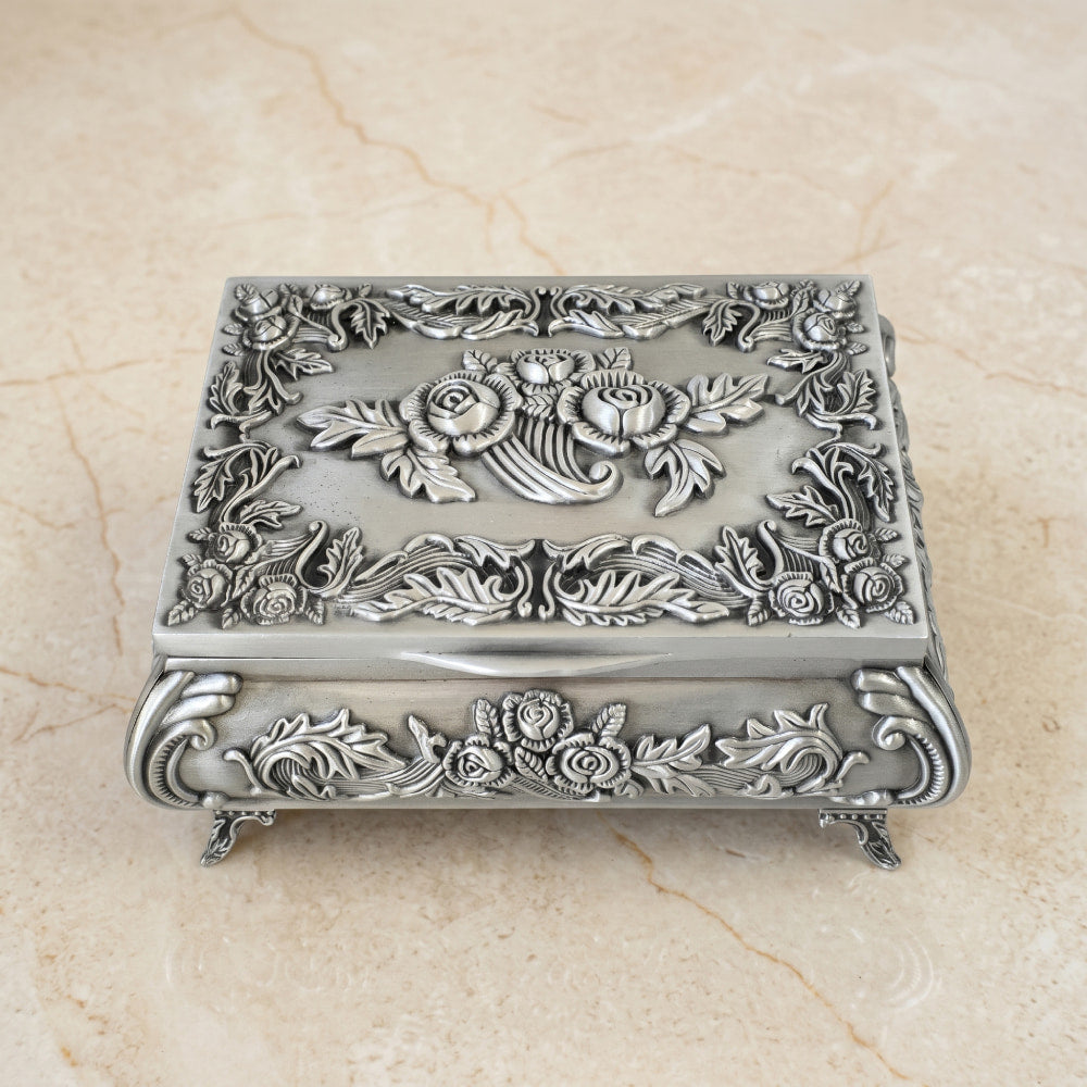 Cofre de pewter con diseño de rosas en relieve y acabado vintage sobre superficie de mármol.