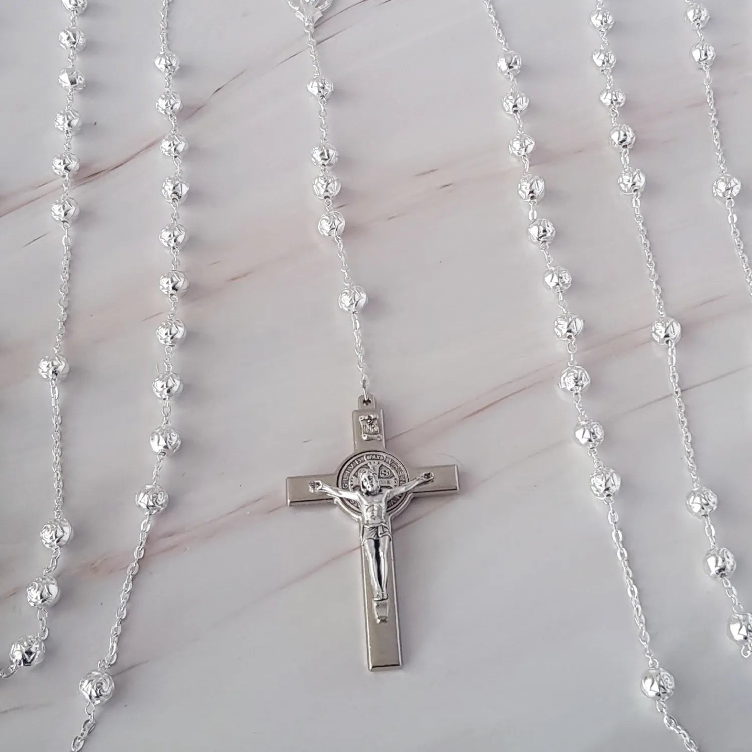 Kit de lazo Rose Silver con estuche de bodas y cruz artesanal nacarada sobre fondo de mármol.