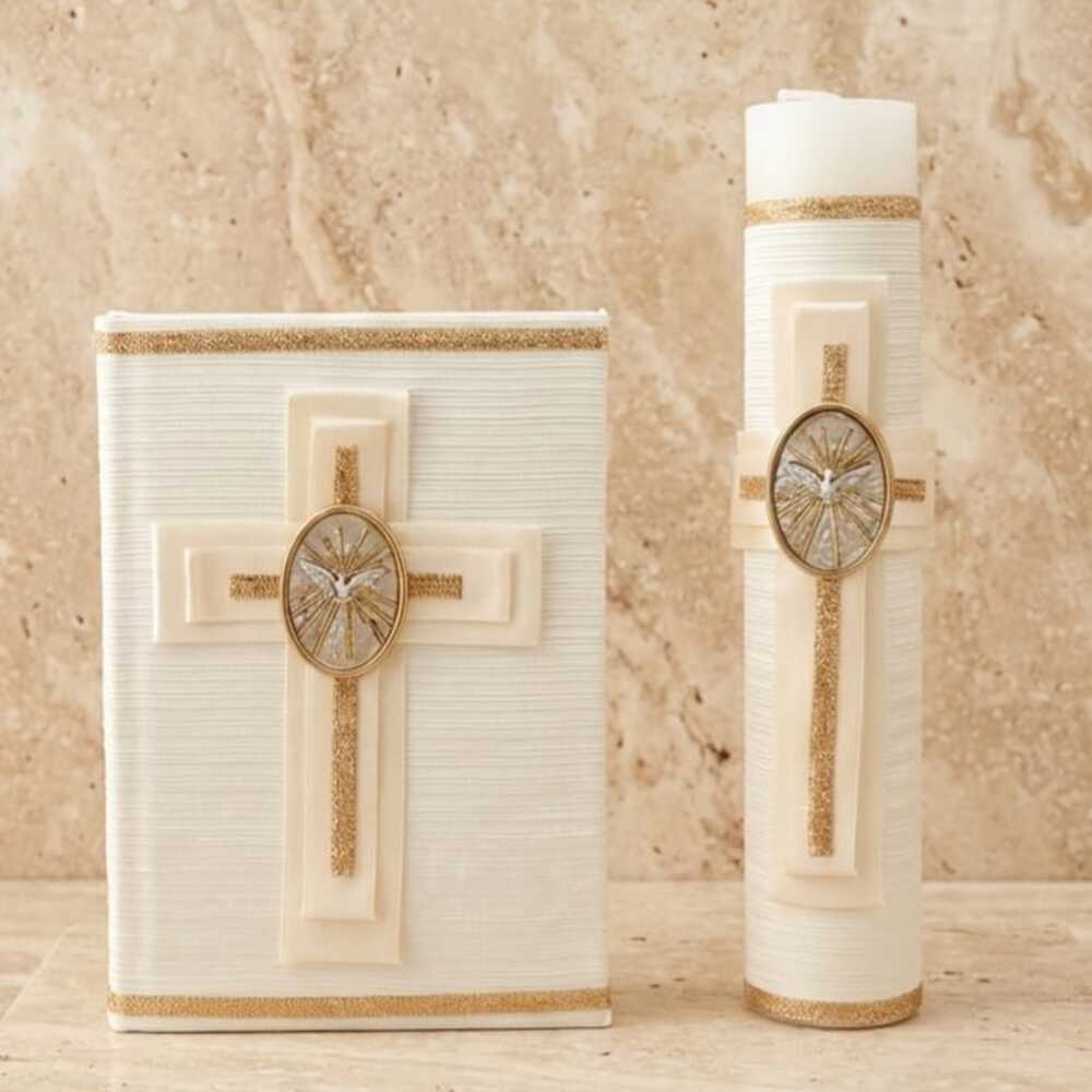Un set religioso sobre una superficie de piedra clara, compuesto por un libro y un cirio grueso de color blanco marfil con textura de líneas horizontales. Ambos elementos están decorados a juego con una cruz en relieve, bordes de purpurina dorada y un medallón ovalado en el centro que muestra una paloma blanca rodeada de rayos dorados, representando al Espíritu Santo.