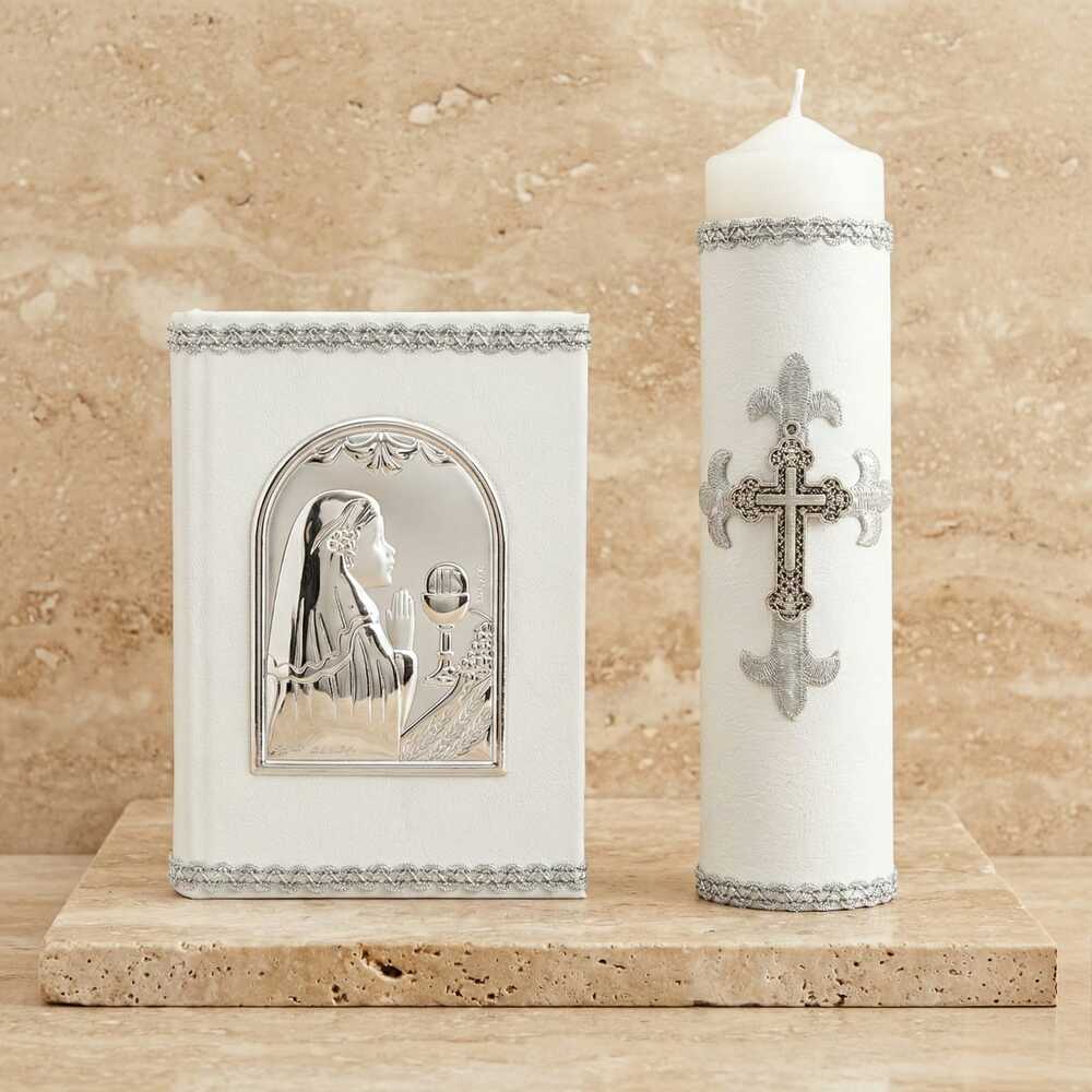 Kit de Primera Comunión blanco con detalles en plata. Incluye libro de oraciones con placa metálica de una niña rezando y cirio decorado con una cruz plateada.