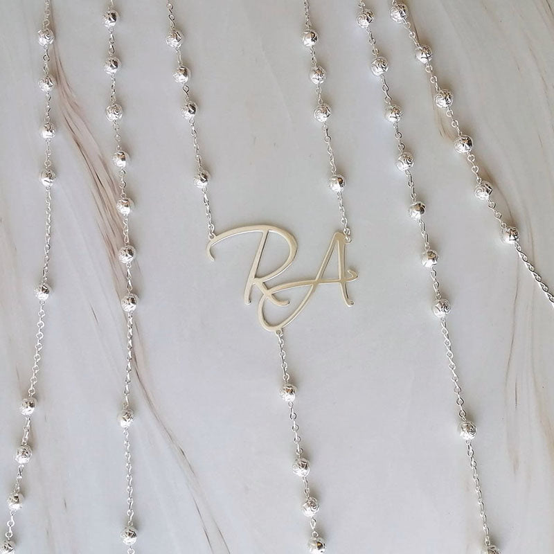 Lazo de boda Rose Silver con cuentas grabadas e iniciales personalizadas de los novios sobre mármol.