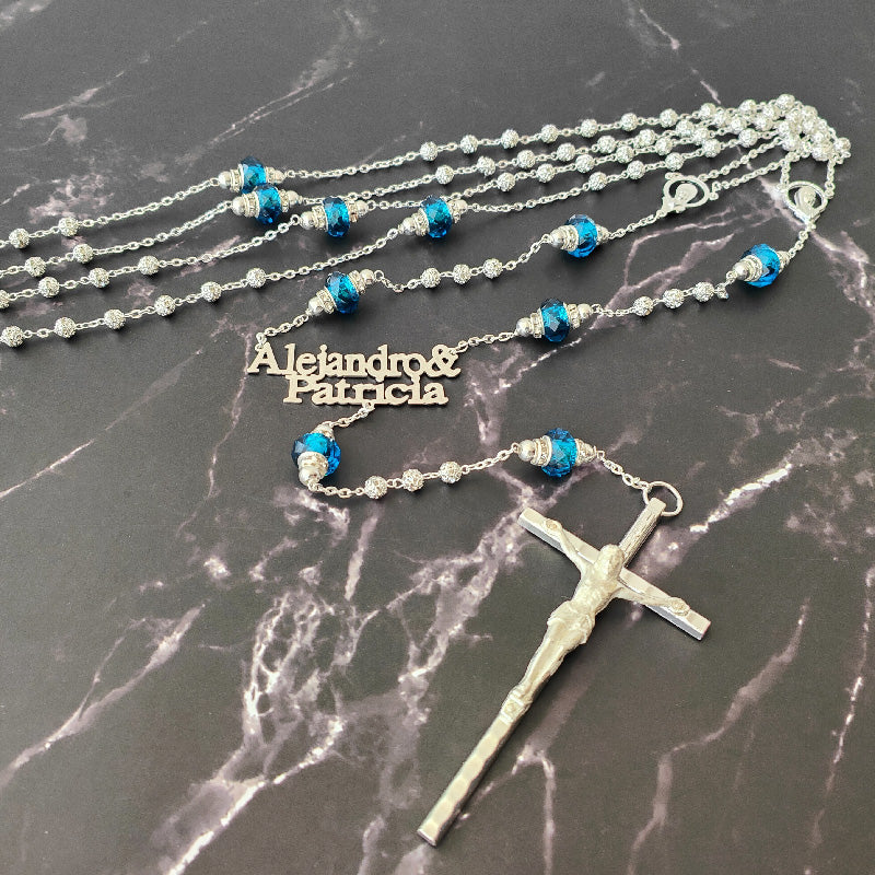 Lazo de boda con cuentas brillantes, cristales azules y nombres personalizados sobre fondo de mármol negro.