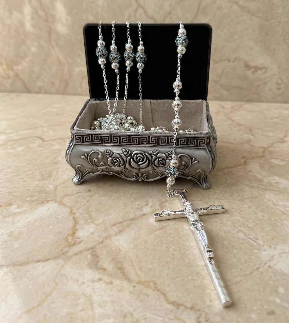 Lazo matrimonial en cofre de plata ornamentado, con cuentas de cristales azules y crucifijo.