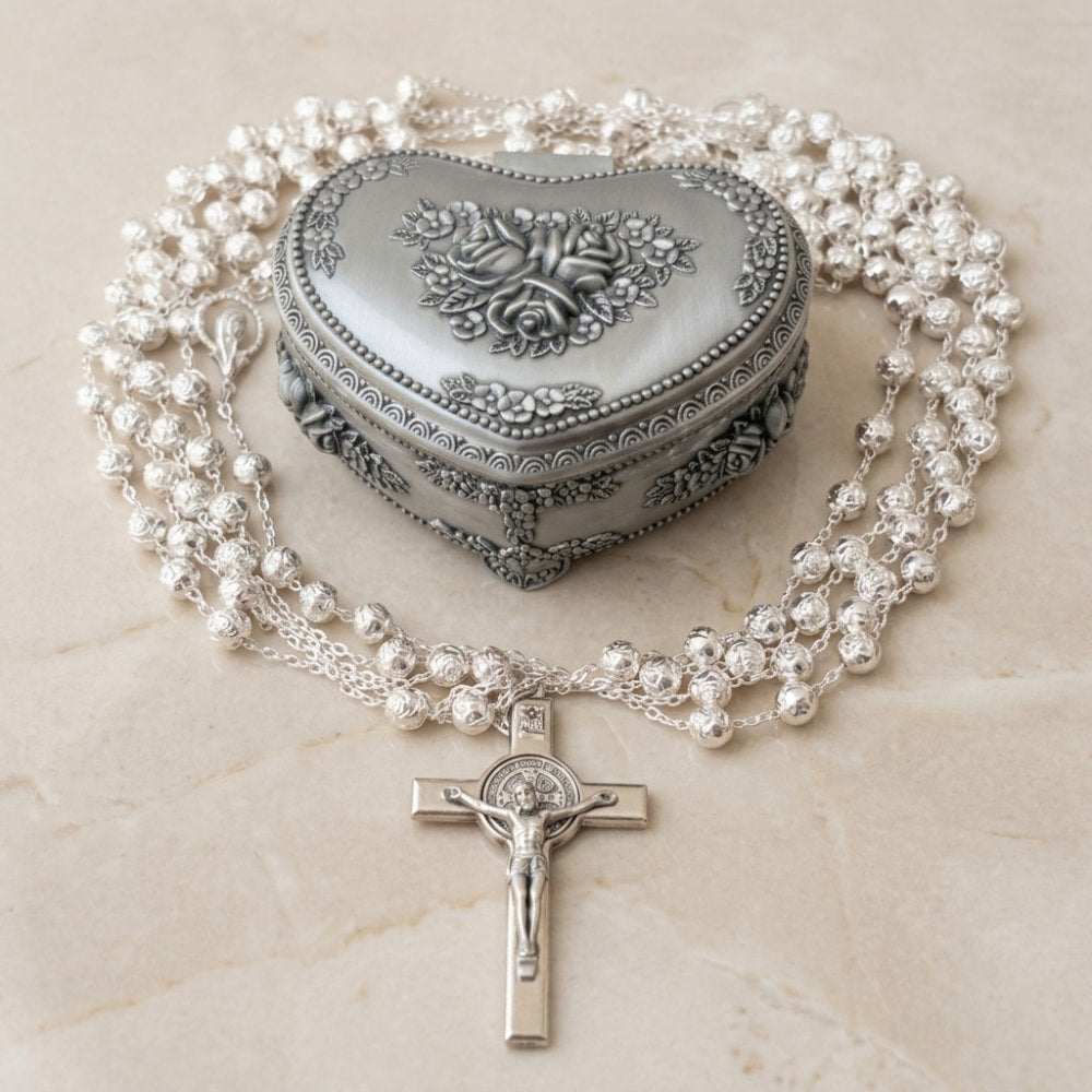 Lazo para boda baño de plata y estuche con rosas de corazón, con cuentas texturizadas y cruz, sobre mármol.