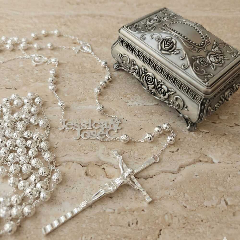 Lazo de boda personalizado en plata con nombres Jessica y Jose, junto a cofre grabado sobre mármol beige.