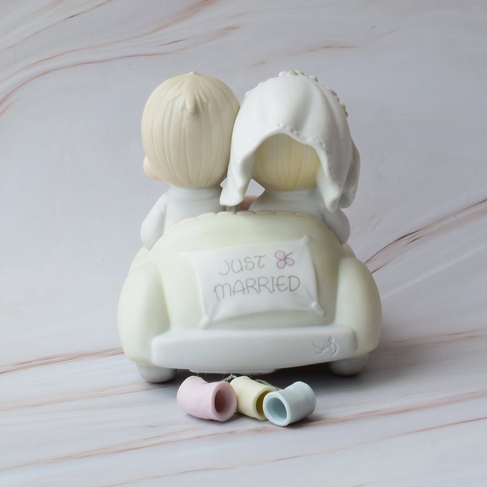 Figura para pastel Precious Moments con novios abrazados, estilo porcelana en tonos suaves, ideal para decoración de bodas elegantes.
