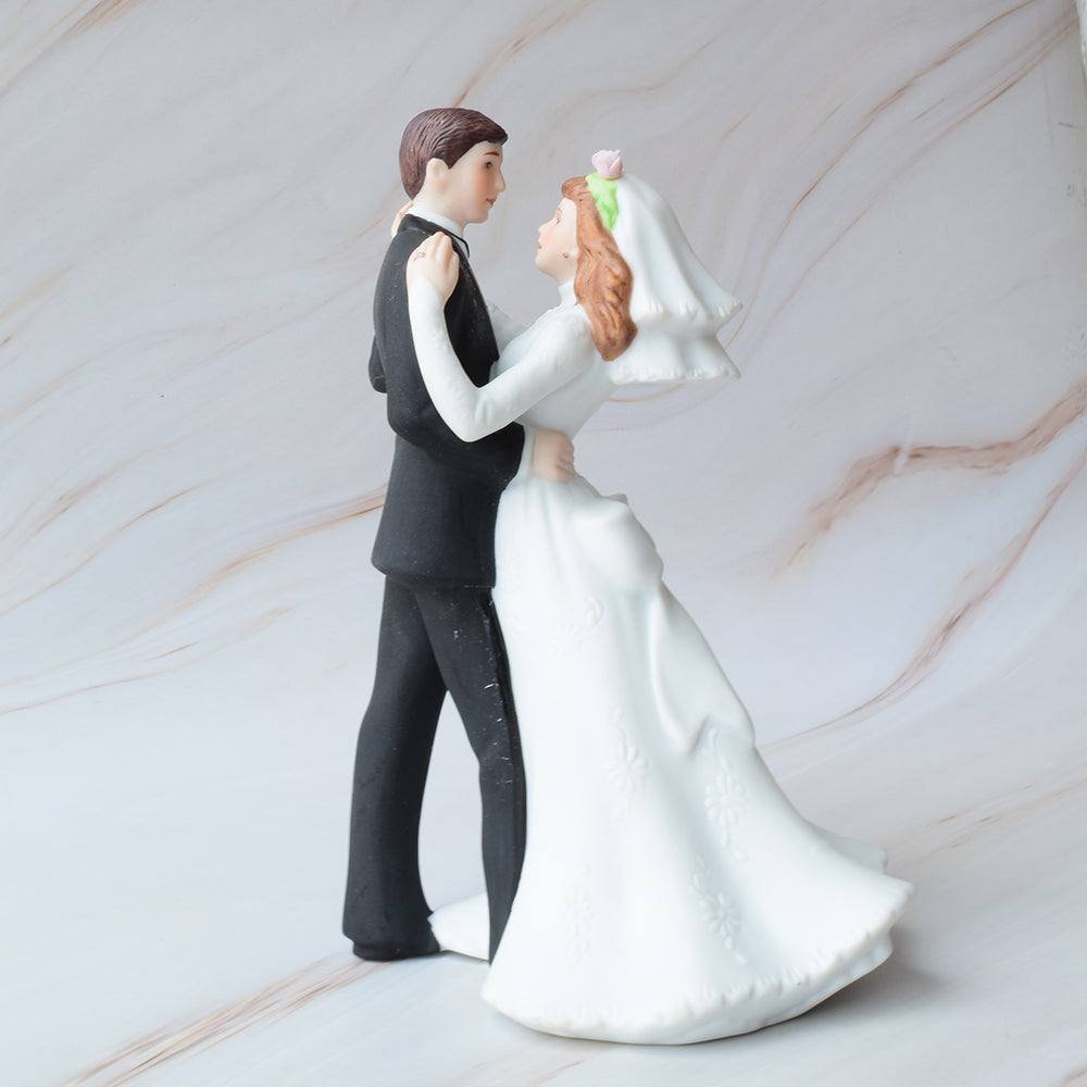 Figura para pastel de boda con novios bailando, ella con vestido de novia detallado y él con traje negro, sobre fondo de mármol.