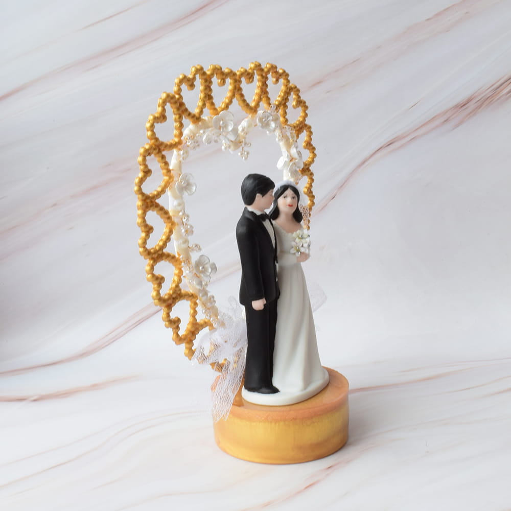 Adorno para pastel de bodas con pareja de novios y arco de corazones dorados.